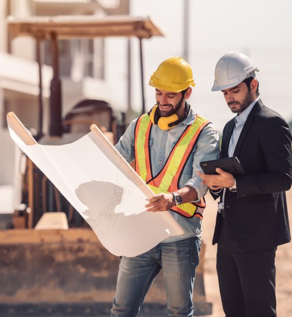 Civil engineer and construction worker manager holding digital tablet and blueprints , talking and planing about construction site.  Cooperation teamwork concept.